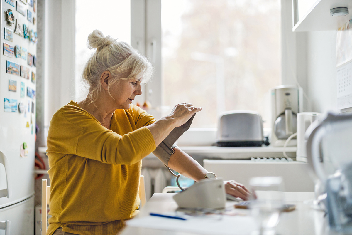 A woman taking her blood pressure in a kitchen